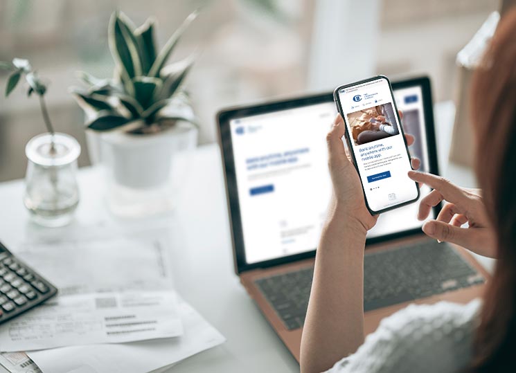 A lady using her laptop computer and smartphone to view The Citizens Bank Company's website in responsive views
