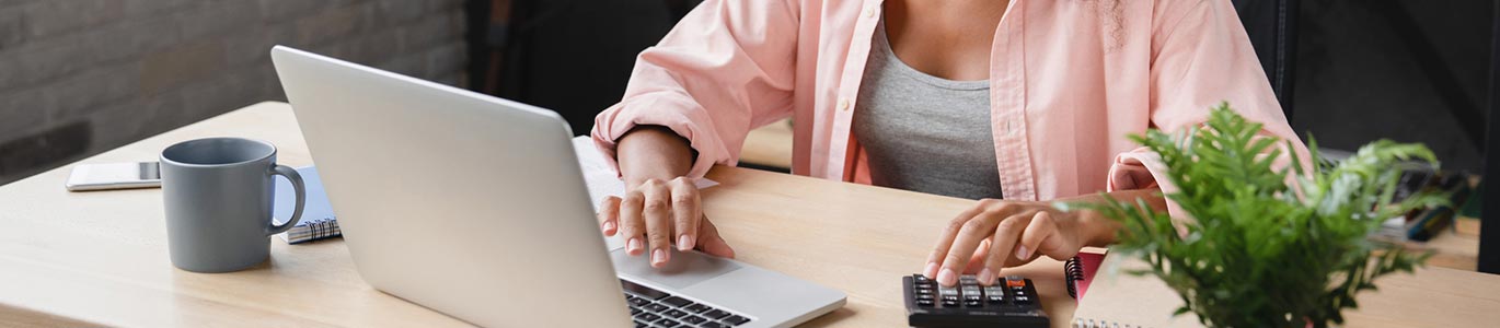 A lady using a calculator and laptop computer at a desk